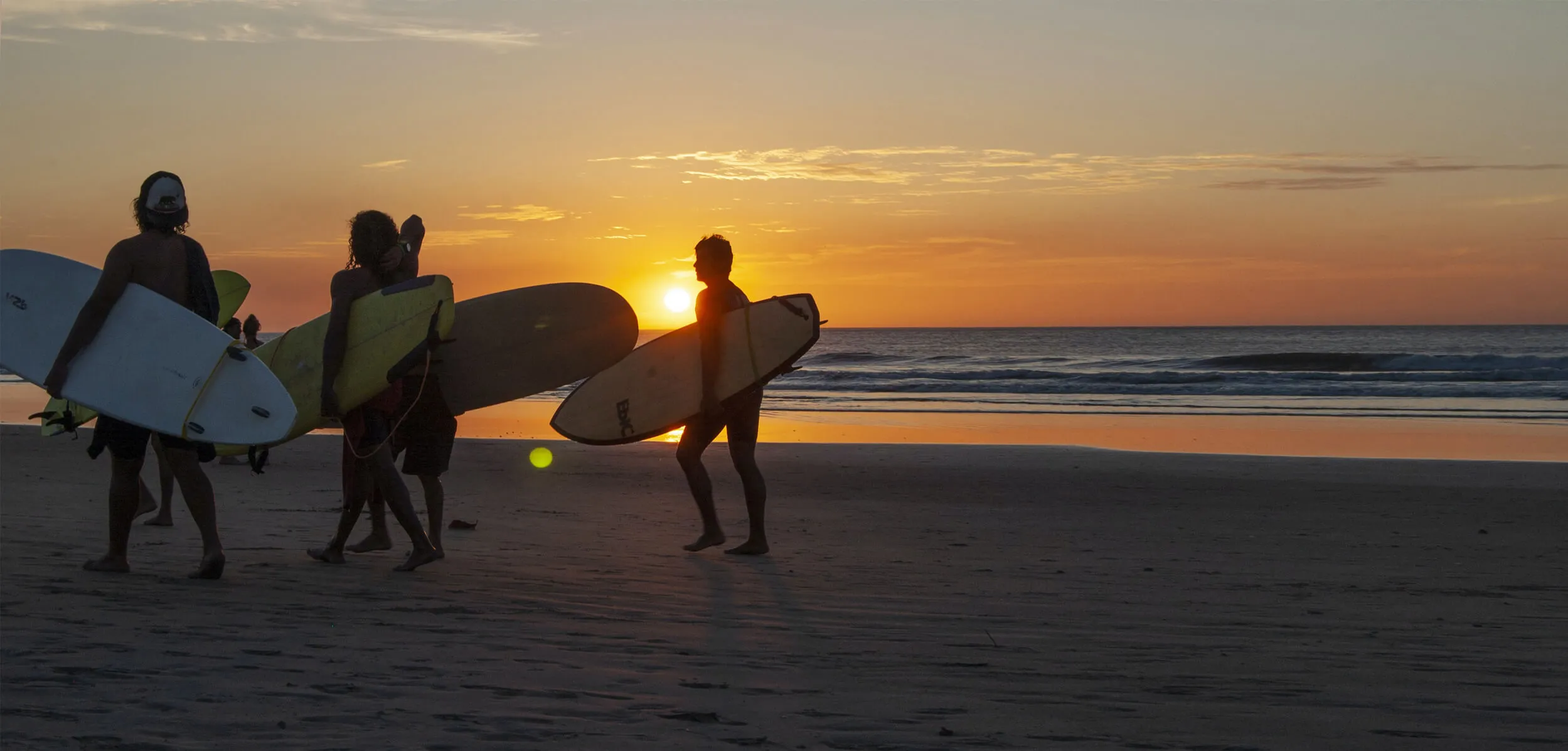 Surfistas caminando por la playa al atardecer
